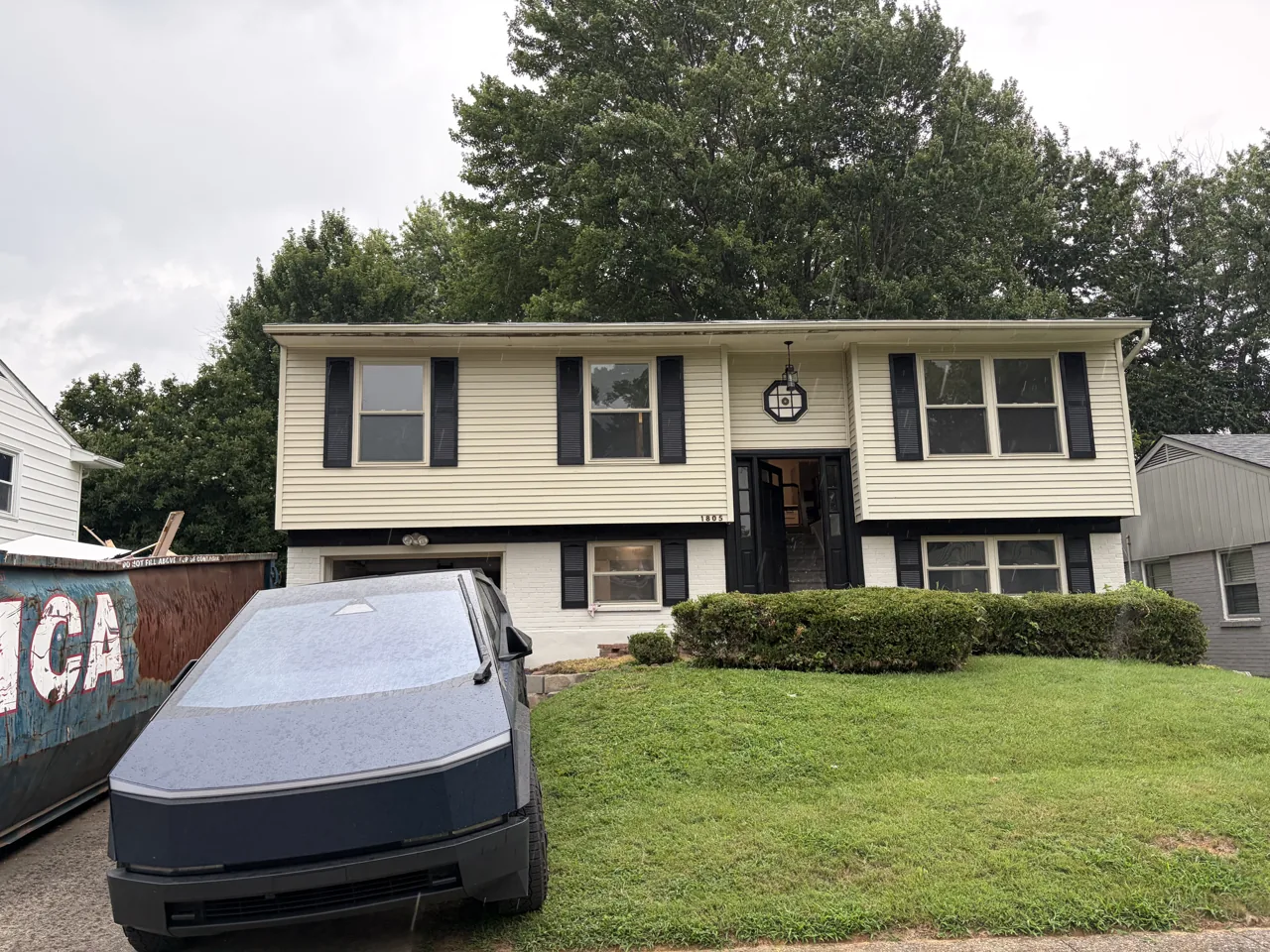 A split-level house with a renovation dumpster and work truck in the driveway.